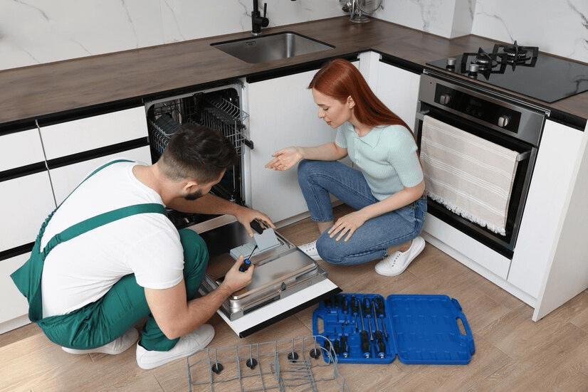 Woman looking how serviceman repairing her dishwasher in kitchen Woman looking how serviceman repairing her dishwasher in kitchen